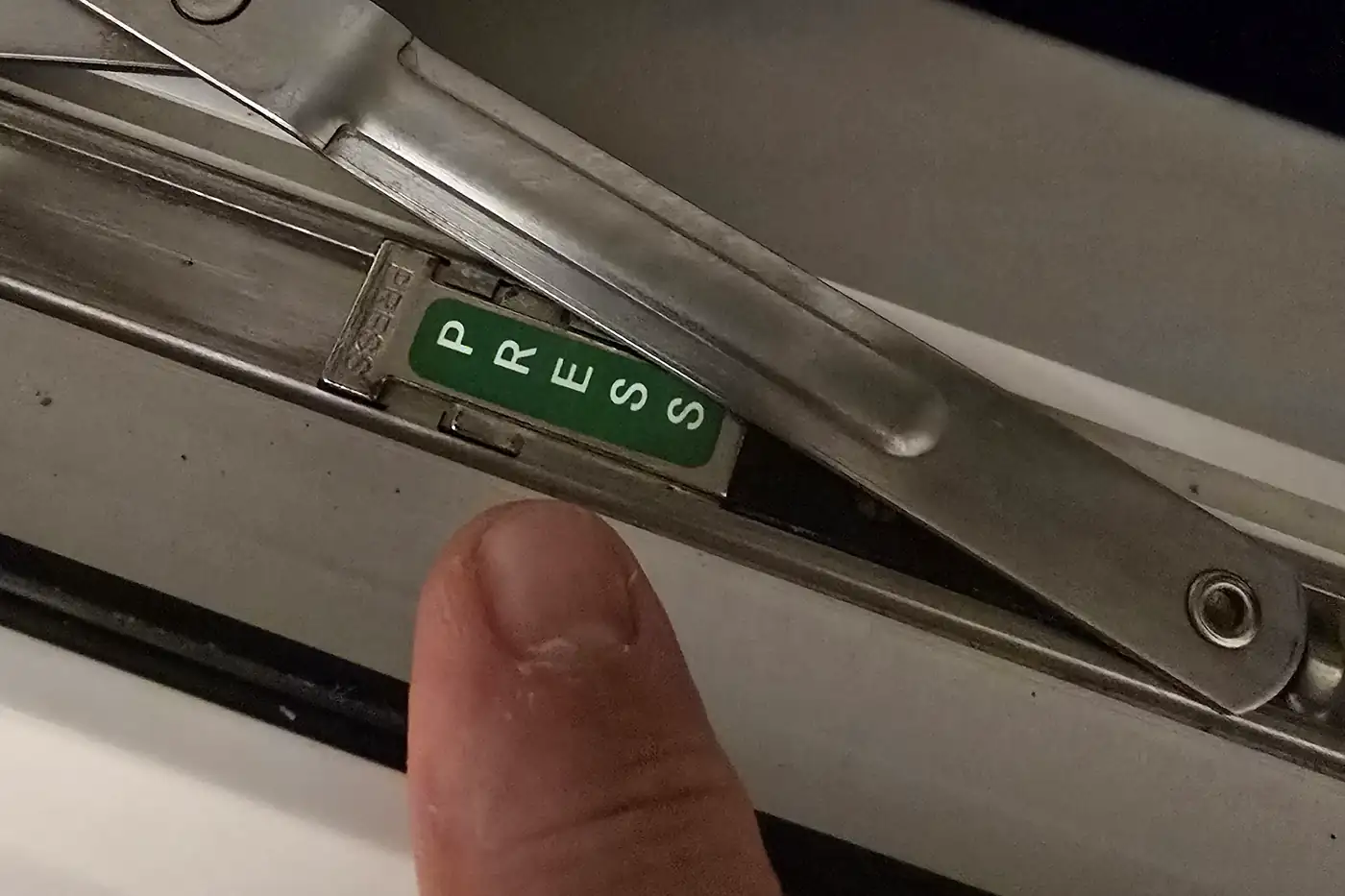 A thumb pressing the green PRESS catch on the window restrictor arm, in the track at the base of a bedroom window